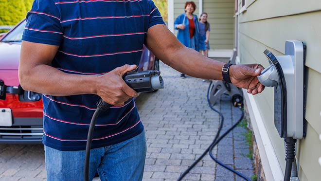 A man plugs an electric charger. The background shows his interracial family walking around and approaching. A man plugs an electric charger. The background shows his interracial family walking around and approaching.